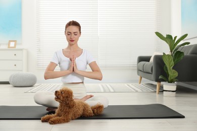 Photo of Young woman practicing yoga on mat with her cute dog at home. Space for text