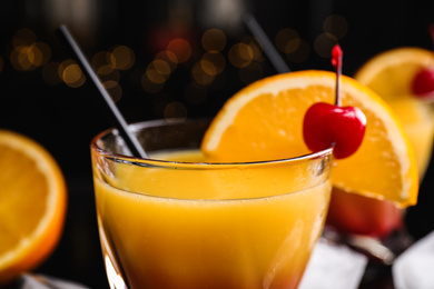 Photo of Fresh alcoholic Tequila Sunrise cocktail against blurred lights, closeup