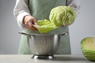 Photo of Woman separate leaf from fresh savoy cabbage at wooden table, closeup