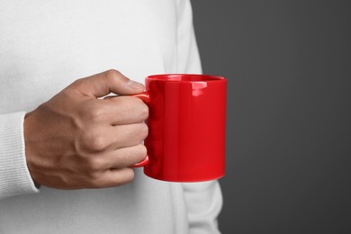 Photo of Man holding red mug on grey background, closeup. Mockup for design