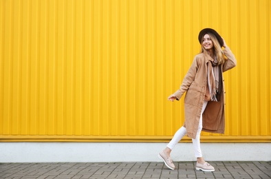 Beautiful young woman in stylish autumn clothes near yellow fence. Space for text