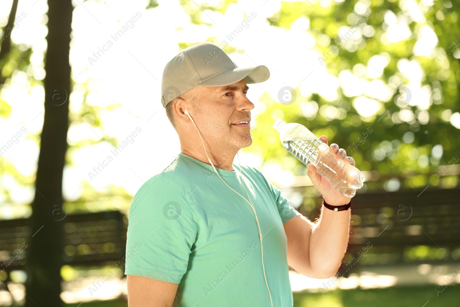 Image of Mature man drinking water after training in park