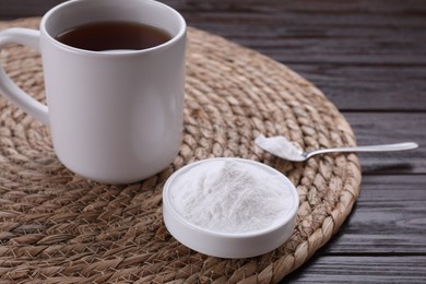 Photo of Bowl of fructose powder and cup with tea on dark wooden table