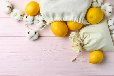 Cotton eco bags with citrus fruits on pink wooden table, flat lay