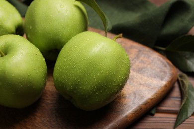 Photo of Ripe green apples with leaves and water drops on wooden table, closeup