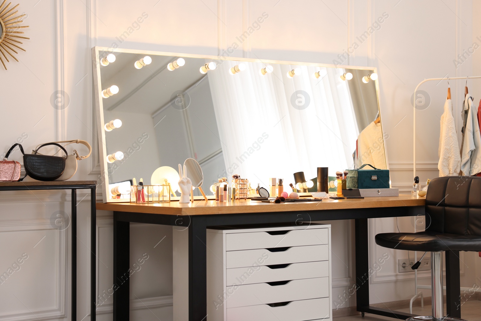 Photo of Makeup room. Stylish dressing table with mirror, chair and clothes rack