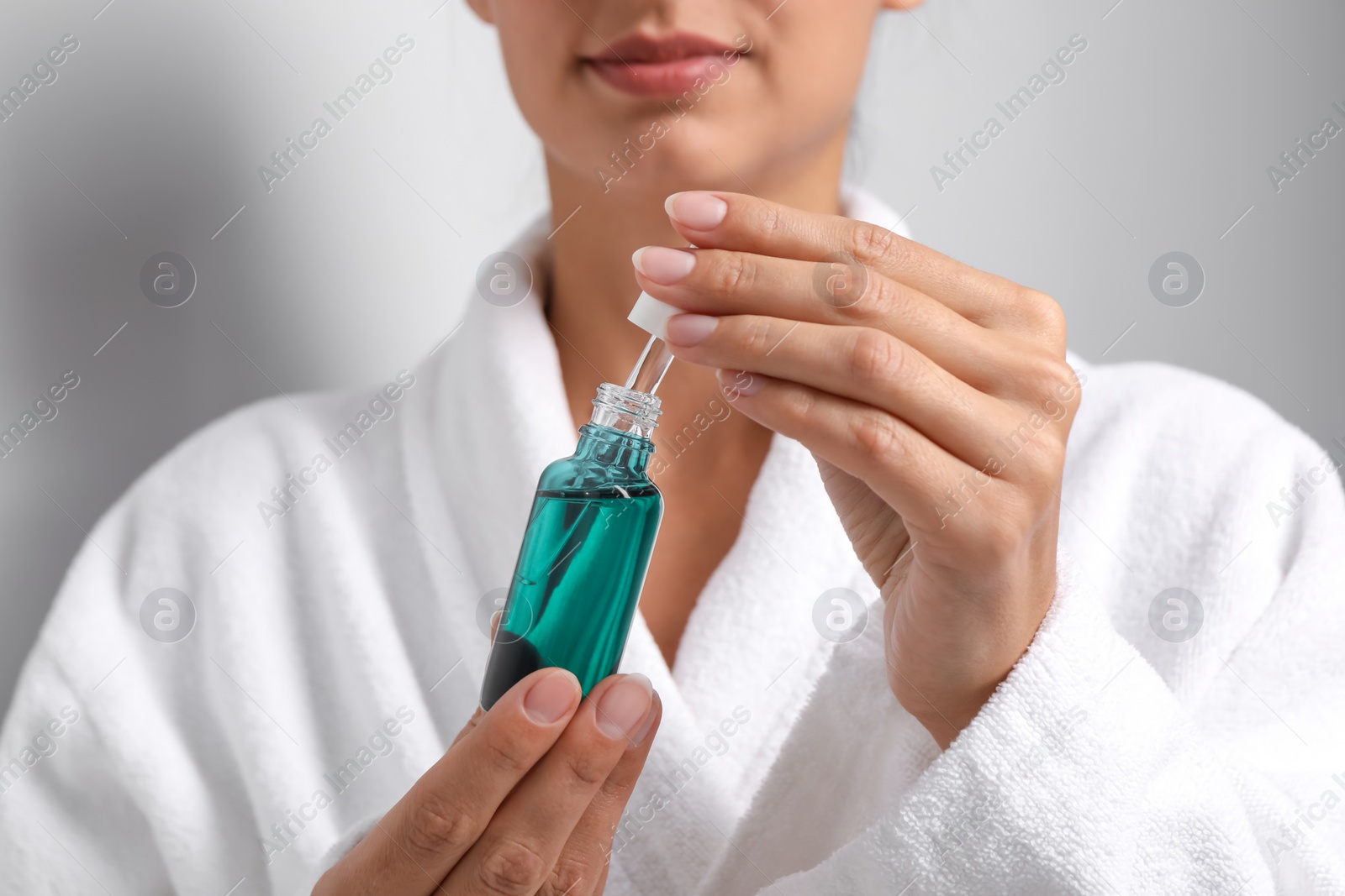 Photo of Woman with bottle of cosmetic serum and pipette on grey background, closeup