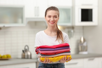 Photo of Woman holding folded clean clothes in kitchen. Laundry day