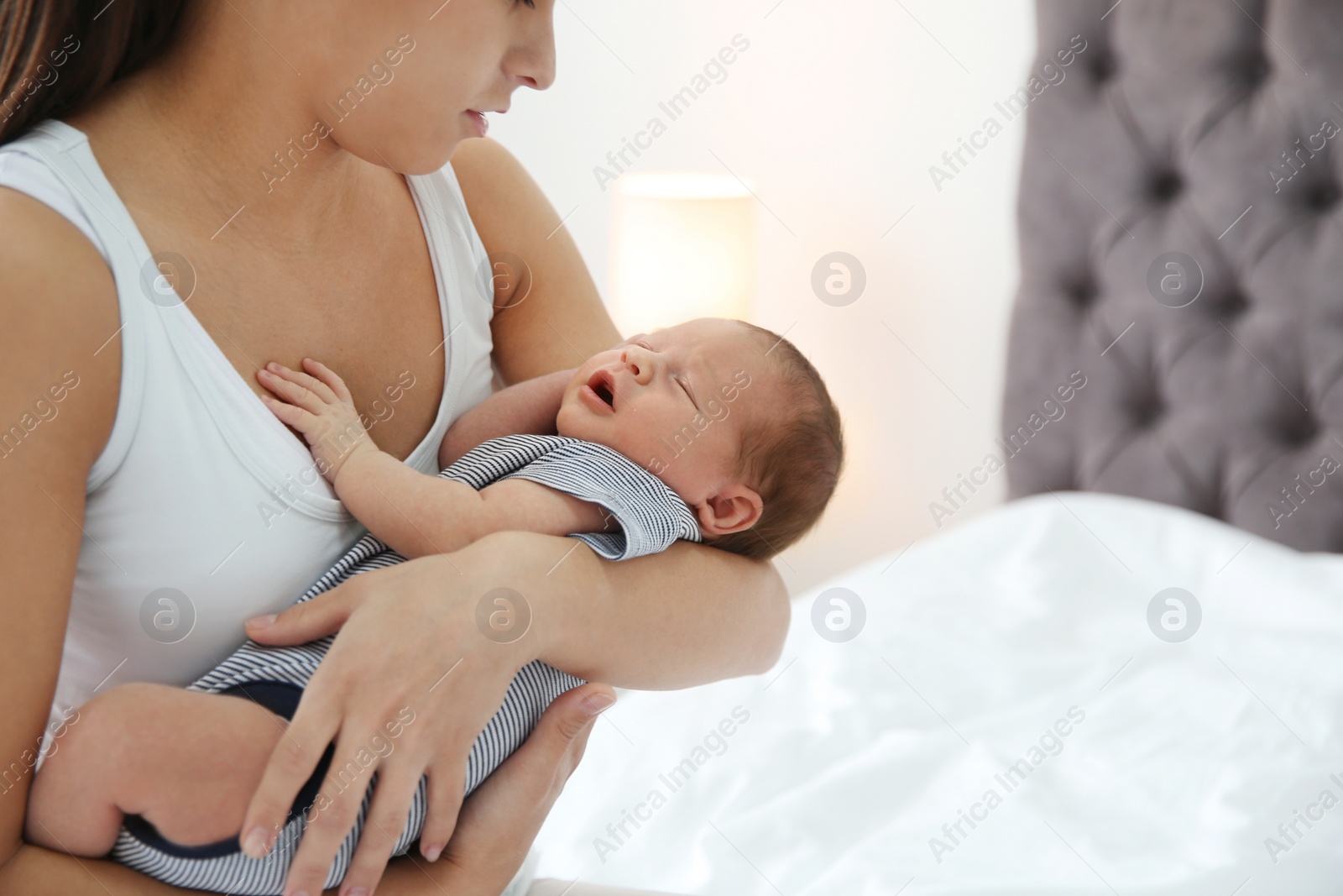 Photo of Young woman holding her baby near breast in bedroom, closeup. Space for text