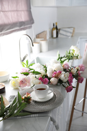 Photo of Beautiful peonies and cup of tea on kitchen counter