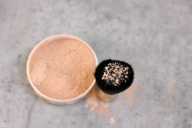 Face powder and brush on grey textured table, top view