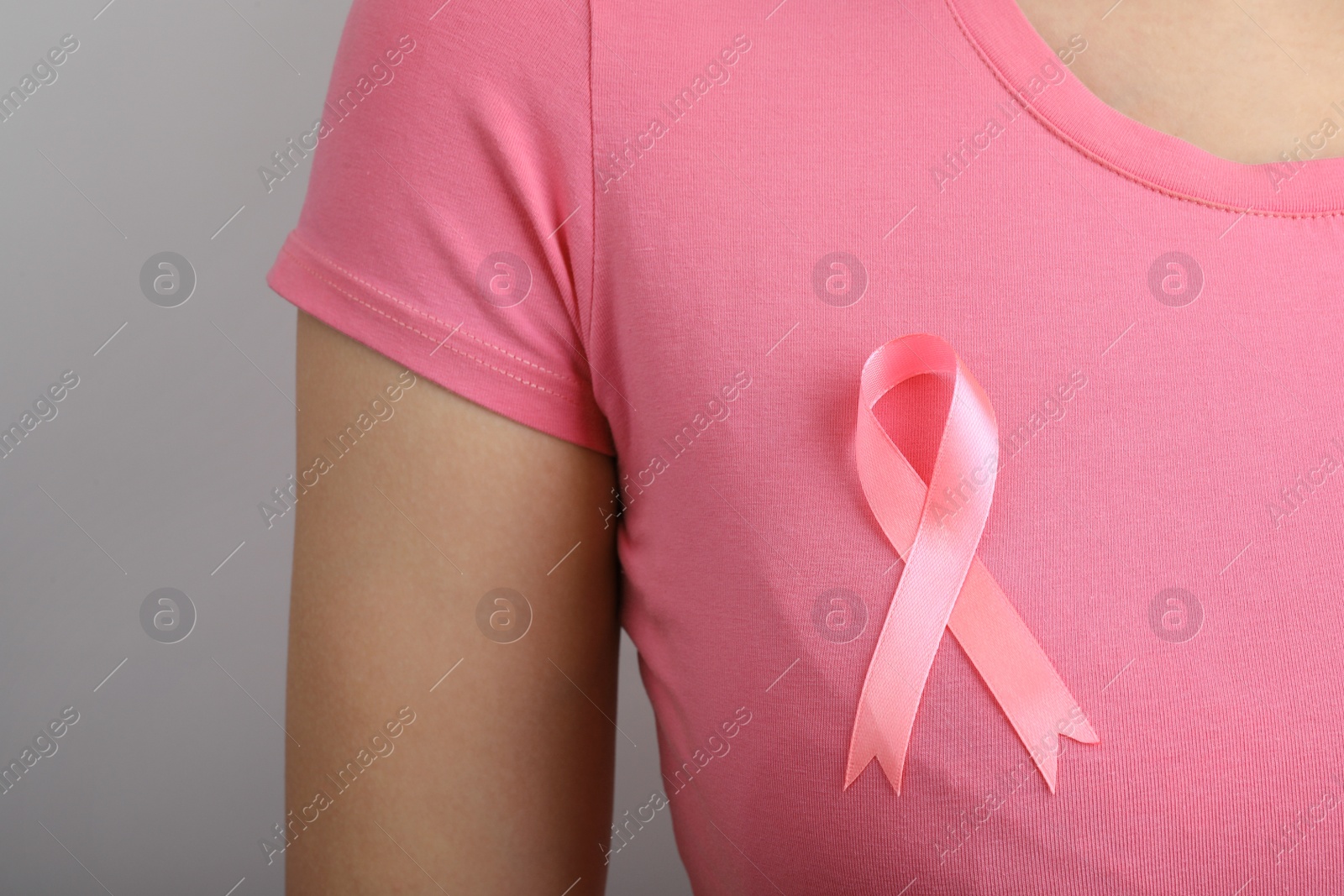 Photo of Woman with pink ribbon on grey background, closeup. Breast cancer awareness