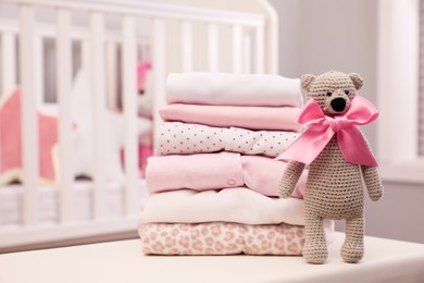 Photo of Stack of clean girl's clothes and toy bear on table