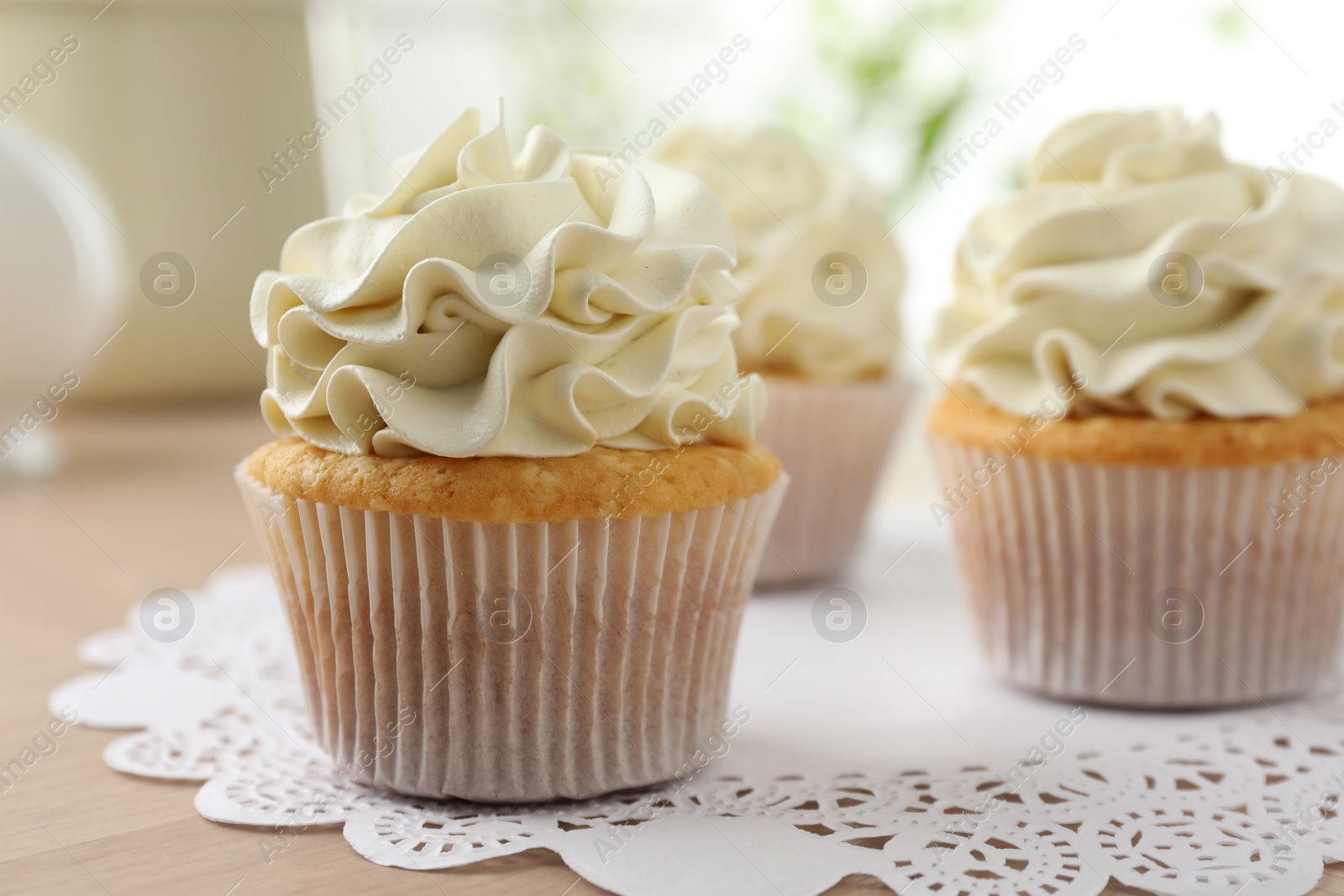 Photo of Tasty cupcakes with vanilla cream on light wooden table, closeup