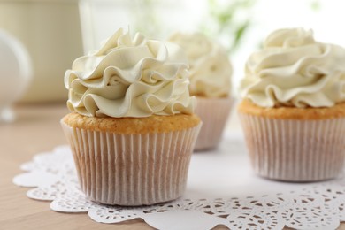 Tasty cupcakes with vanilla cream on light wooden table, closeup