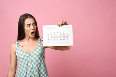 Photo of Young woman holding calendar with marked menstrual cycle days on pink background