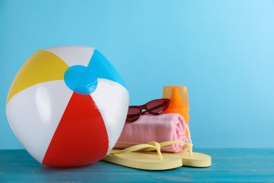 Photo of Colorful inflatable ball and beach accessories on light blue wooden table. Space for text