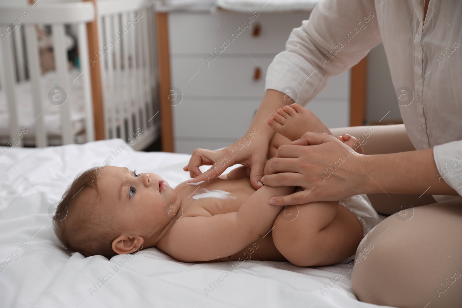 Photo of Mother applying moisturizing cream on her little baby at home, closeup