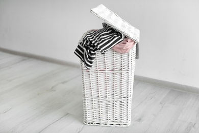 Laundry basket with dirty clothes on floor near light wall