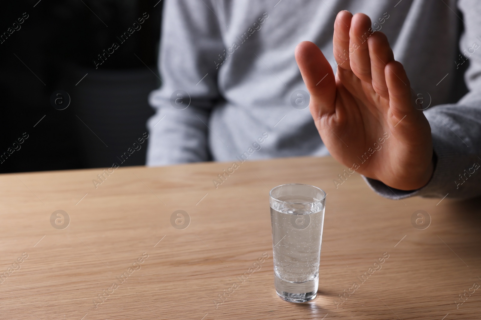 Photo of Man refusing to drink vodka at wooden table, closeup. Alcohol addiction