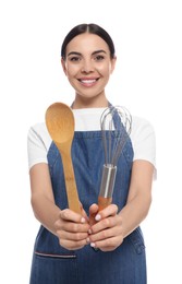 Photo of Young woman in blue jeans apron holding wooden spoon and whisk on white background