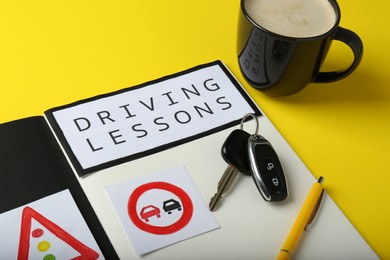 Photo of Workbook for driving lessons, cup of coffee and keys on yellow background. Passing license exam
