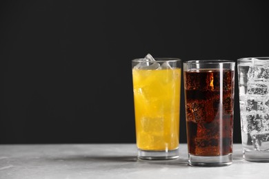 Glasses of different refreshing soda water with ice cubes on white marble table, space for text