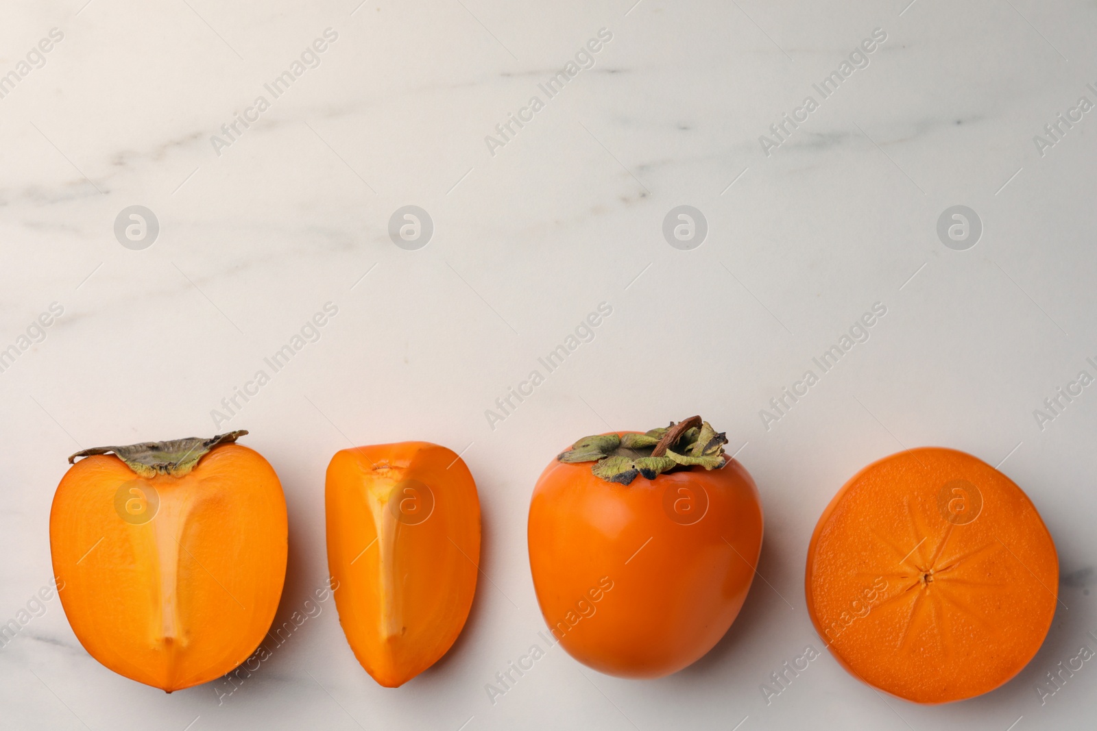 Photo of Delicious ripe persimmons on white marble table, flat lay. Space for text