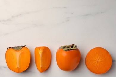 Delicious ripe persimmons on white marble table, flat lay. Space for text