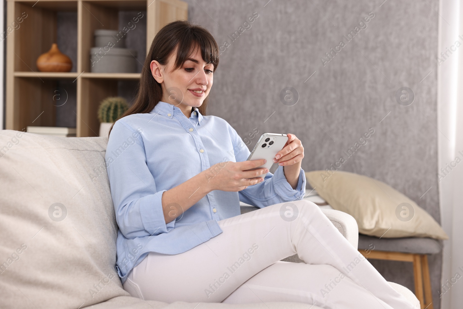 Photo of Beautiful young housewife using smartphone on sofa at home