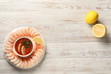 Photo of Tasty boiled shrimps with cocktail sauce and lemon on white wooden table, top view. Space for text