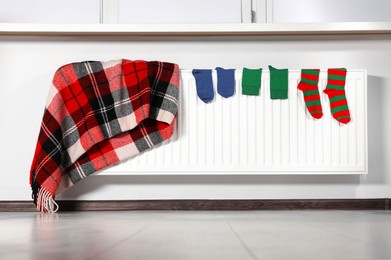 Checkered blanket and different colorful socks hanging on white radiator in room