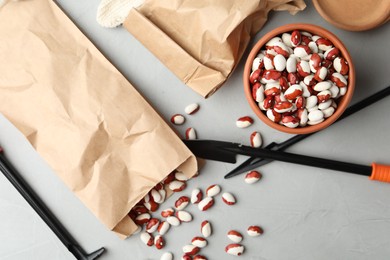 Photo of Paper bag with raw beans and gardening tools on grey table, flat lay. Vegetable seeds