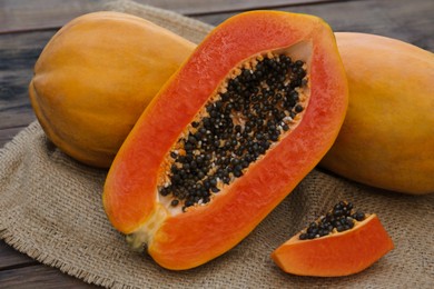 Photo of Tasty cut and whole papaya fruits on wooden table, closeup