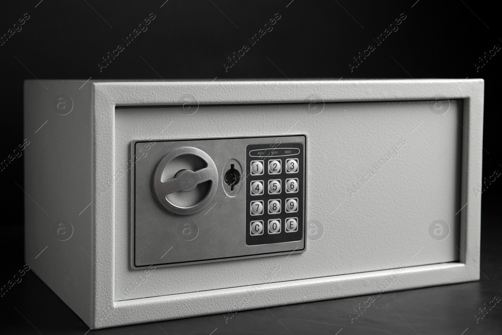 Photo of Steel safe with electronic lock on grey table against black background, closeup view