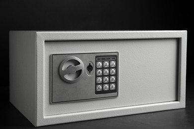 Photo of Steel safe with electronic lock on grey table against black background, closeup view