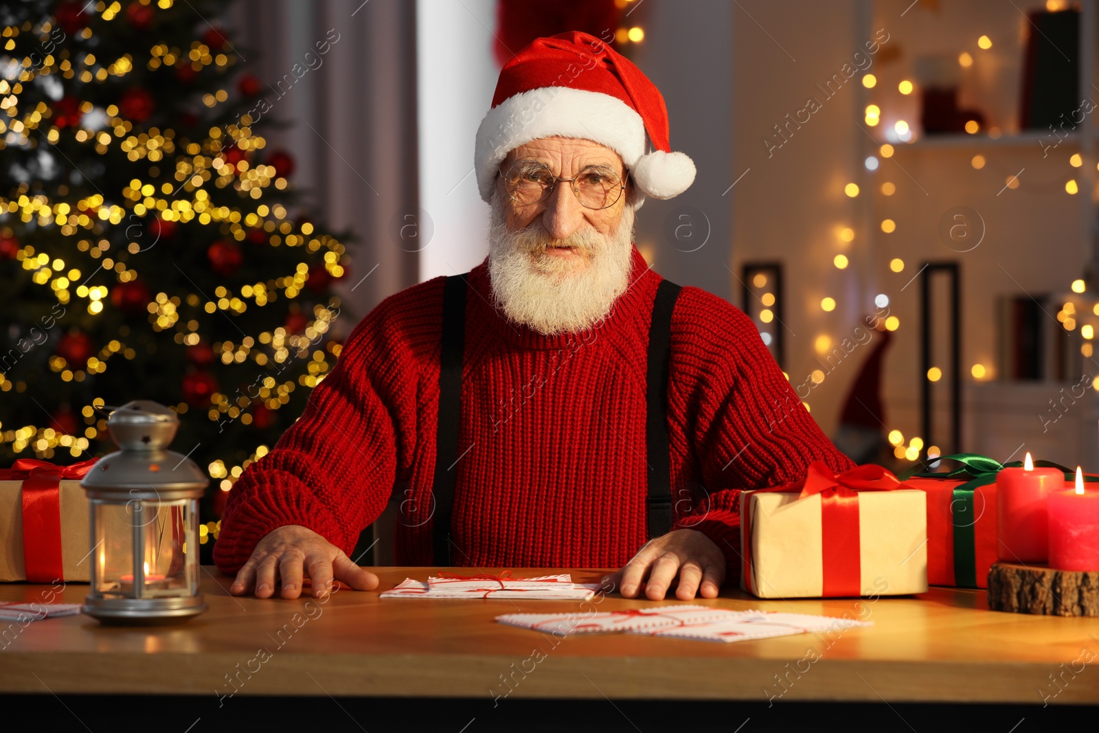 Photo of Santa Claus at his workplace. Letters and gift boxes on table in room with Christmas tree