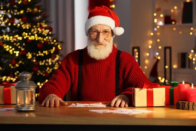 Santa Claus at his workplace. Letters and gift boxes on table in room with Christmas tree