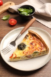 Photo of Piece of delicious homemade vegetable quiche and fork on wooden table