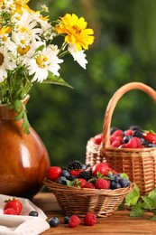 Photo of Different fresh ripe berries and beautiful flowers on wooden table outdoors