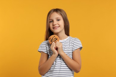 Photo of Cute girl with chocolate chip cookie on orange background