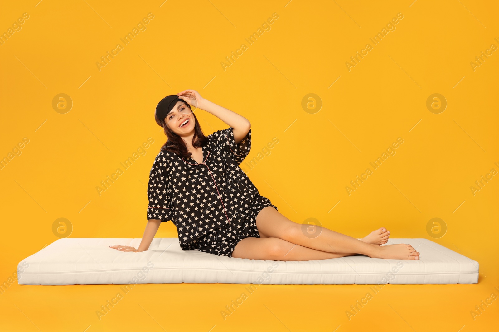 Photo of Woman in sleep mask sitting on soft mattress against orange background