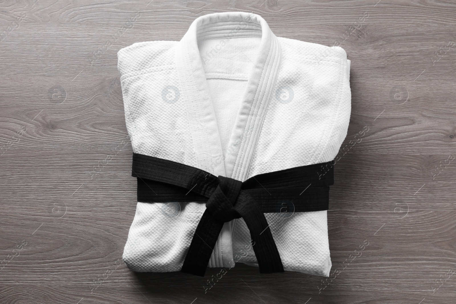 Photo of Martial arts uniform with black belt on wooden background, top view