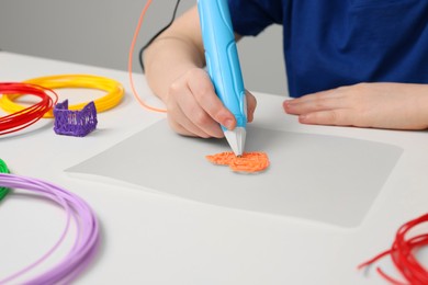 Boy drawing with stylish 3D pen at white table, closeup