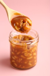 Photo of Taking tasty salted caramel with peanuts from jar on pink background, closeup