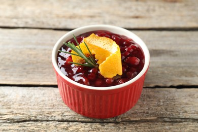 Photo of Fresh cranberry sauce in bowl, rosemary and orange peel on wooden table, closeup