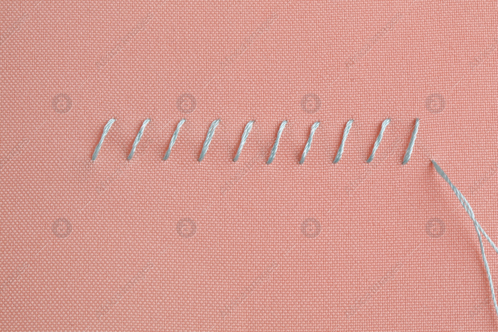 Photo of Sewing thread and stitches on coral cloth, top view