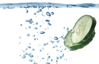 Photo of Slices of fresh cucumber in glass with water on white background, closeup