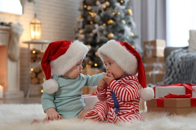 Cute children in Santa hats on floor in room with Christmas tree