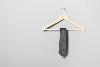Hanger with necktie on light grey wall. Space for text